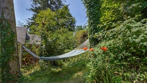 A hammock in a lush garden with a stone wall and a tree.
