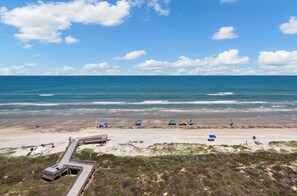 A beach with a wooden boardwalk, tents, and a clear blue sky.