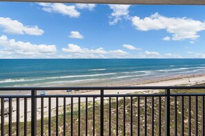 A beach view from a balcony with a railing, ocean, and clear sky.
