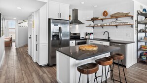 A modern kitchen with white cabinets, stainless steel appliances, and a central island with stools. - Sea Gull #907: Beachfront 2 Bedroom 2 Bathroom With Spectacular Views and 24 Hour Management (Port Aransas)