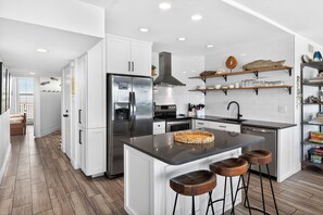 A modern kitchen with white cabinetry, stainless steel appliances, and a central island with stools.