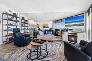 Ein modernes Wohnzimmer mit Kamin, einer Couch, einem Esstisch und Blick auf den Strand durch große Fenster.