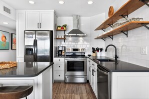A modern kitchen with white cabinets, stainless steel appliances, and wooden shelves.