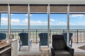 Un balcon avec vue sur l’océan, des chaises bleues, une petite table ronde et une horloge.