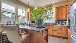 A kitchen with wooden cabinets, a large island with a plant, hanging pendant lights, and a refrigerator. - Wine Country Home with Yard; Walk to Downtown! (Walla Walla)
