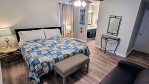 Une chambre à coucher avec un lit, un banc, une table de chevet, une lampe et un miroir au mur.