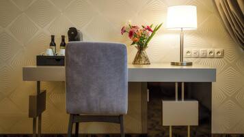 Habitación de hotel con escritorio, una silla, lámpara, un jarrón con flores y un minibar.