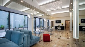 A modern lobby with a blue sofa, red ottoman, and glass tables. - Hotel Essence  (Prague)