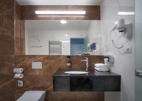 Um banheiro moderno com toucador de mármore, um espelho grande, porta-toalhas e um secador de cabelo fixado na parede.