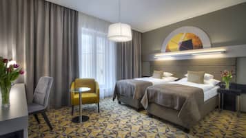 A hotel room with two beds, a desk, a chair, and a large window with curtains.
