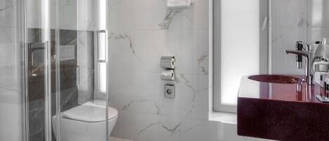 A modern bathroom with a glass-enclosed shower, a white toilet, and a marble-tiled floor.