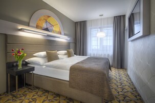 Camera d'albergo con un letto grande, un comodino con un vaso di fiori e una finestra con tende.