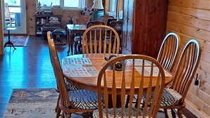 A dining area with a wooden table and chairs, a patterned rug, and a view of the outdoors through large windows. - Blue Mountain Cottage near Deep Creek Campground (Bryson City)
