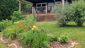 A house with a covered porch, surrounded by a garden with various plants and flowers. - Blue Mountain Cottage near Deep Creek Campground (Bryson City)