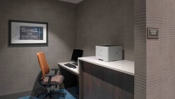 Centro de negocios con un cartel de bienvenida enmarcado, un escritorio de ordenador con monitor, teclado e impresora, y una silla de oficina moderna.