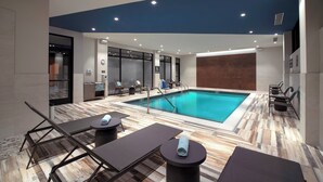 A modern indoor pool area with lounge chairs and a pool table, surrounded by a wooden floor and a blue ceiling.