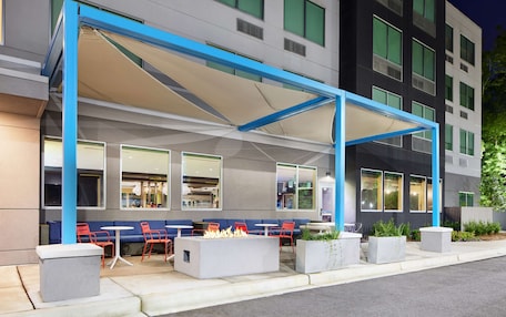 An outdoor seating area with a fire pit, red chairs, and a blue canopy.