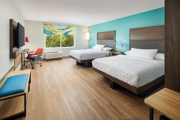 Quarto de hotel com duas camas, uma escrivaninha, uma cadeira, uma televisão e janela com vista para o verde.