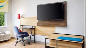 Una habitación moderna con televisor de pantalla plana montado en la pared, un escritorio con una silla, un banco con cojín y una lámpara roja.