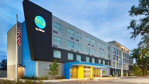 Un moderno edificio de hotel con un llamativo letrero de 'TRU by Hilton', ventanas amplias y una entrada bien iluminada.