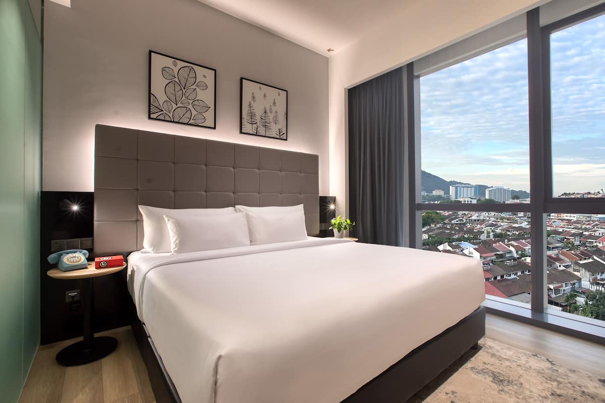 Une chambre d’hôtel moderne dotée d’un grand lit, d’une table de chevet avec un téléphone et offrant une vue sur le paysage urbain grâce à de grandes fenêtres.