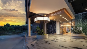 Una entrada de hotel moderna con un toldo curvo, plantas en macetas grandes y un letrero que dice "INNSIDE".