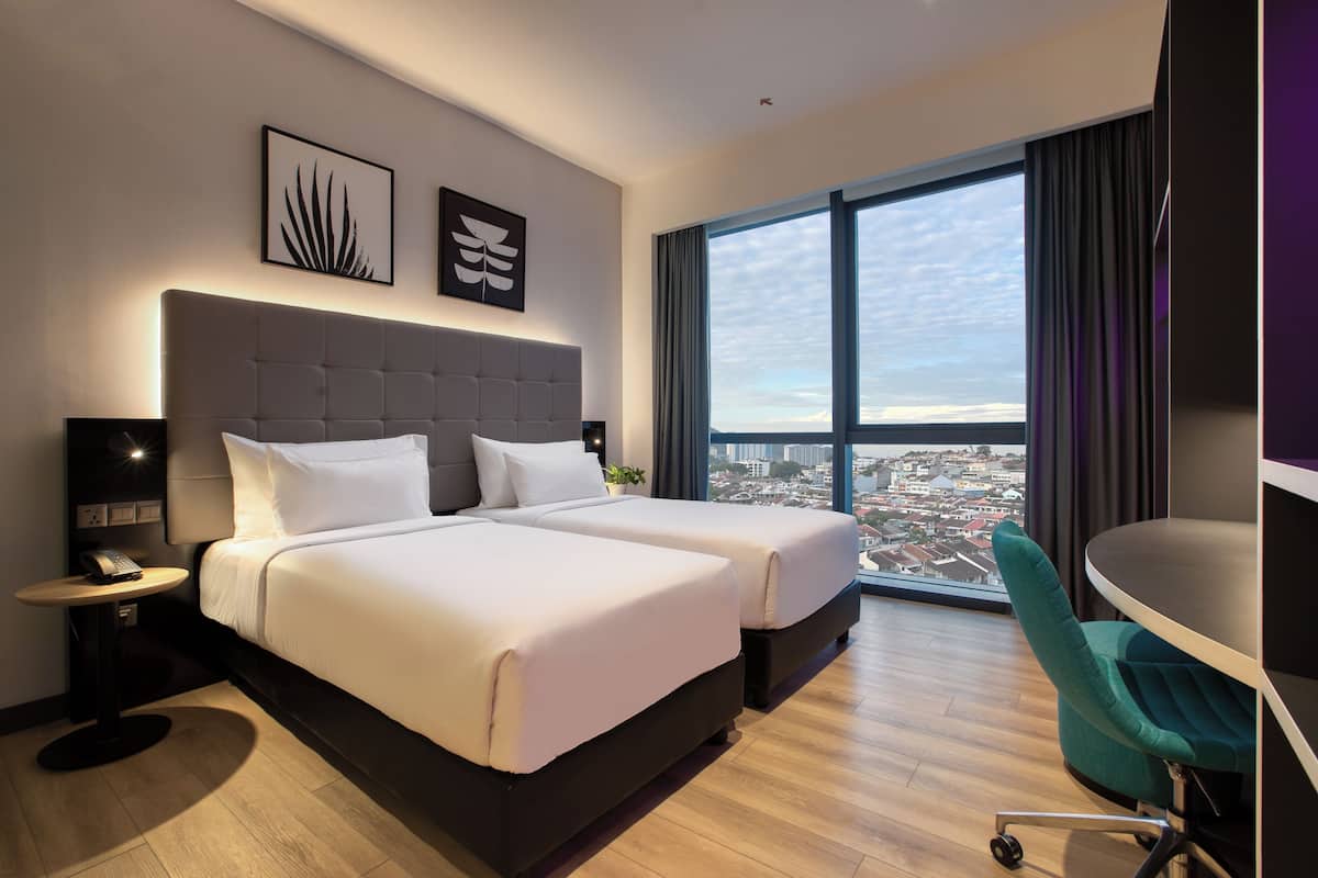 Une chambre d’hôtel moderne avec deux lits, un bureau et une grande fenêtre donnant sur la ville.