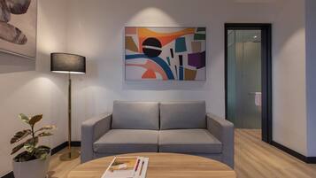 A modern interior with a grey sofa, a round wooden coffee table with a magazine, a floor lamp, and a colorful abstract painting on the wall.