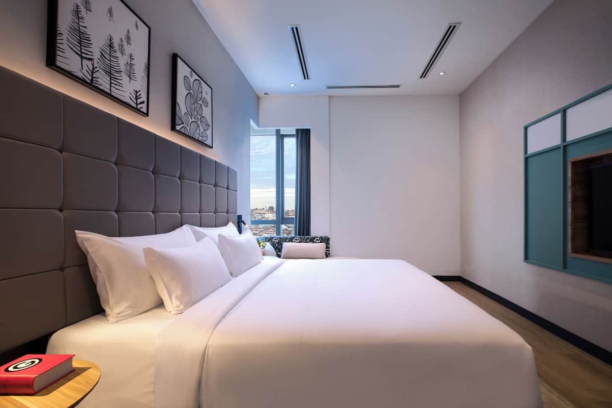 Une chambre d’hôtel moderne avec un grand lit, une tête de lit et une vue sur la ville grâce à une grande fenêtre.