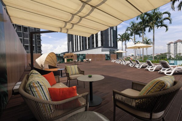A rooftop lounge area with wicker furniture, a pool, palm trees, and a modern building in the background. -  INNSiDE by Meliá Kuala Lumpur Cheras (Kuala Lumpur)