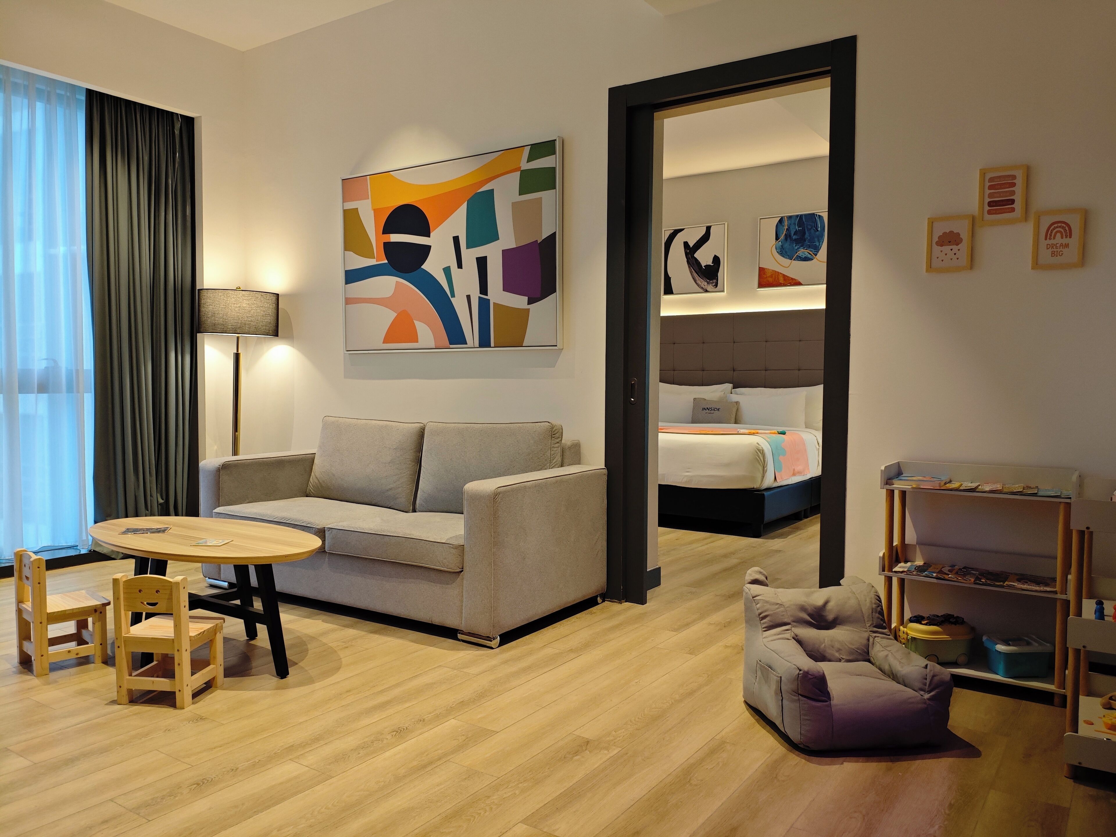 Ein modernes Hotelzimmer mit einer Couch, einem runden Holztisch, einem violetten Sessel und einem Bett mit Kopfteil.