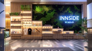 Un espace commercial moderne avec des étagères en bois où sont exposés divers articles, une grande enseigne lumineuse indiquant « INNSiDE BY MELIA » et un sol poli.