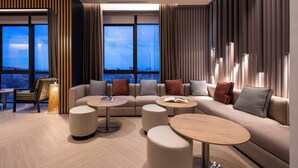 Una sala de estar moderna con un sofá grande, mesas de centro redondas y vistas de la ciudad al anochecer.
