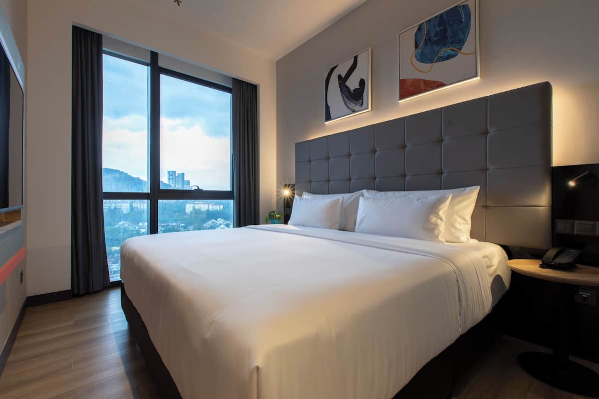Une chambre d’hôtel avec un grand lit, une vue sur la ville par la fenêtre et une tête de lit moderne.