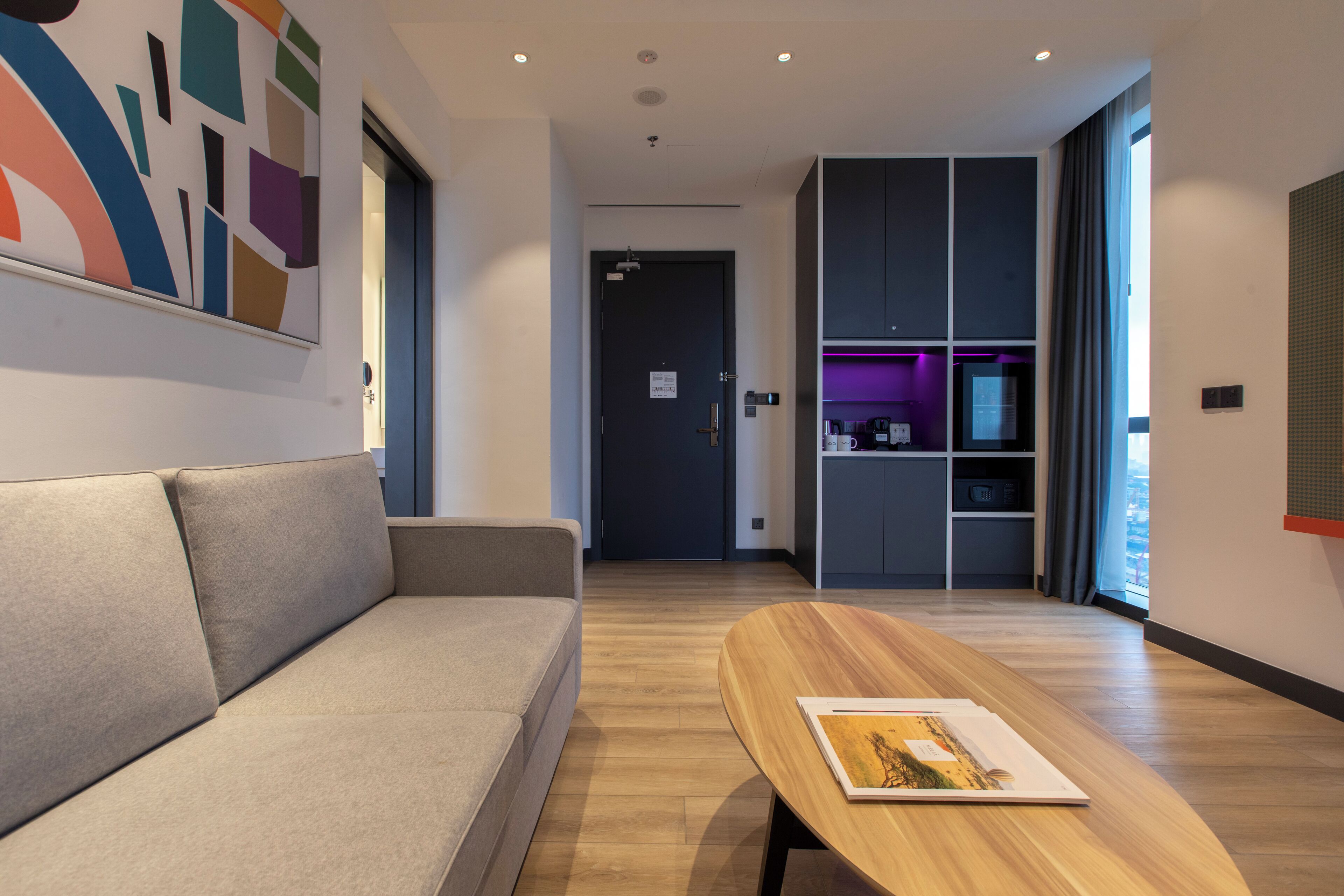 Ein modernes Wohnzimmer mit einer Couch, einem Holztisch und einer Küchenzeile mit einem violett beleuchteten Schrank.