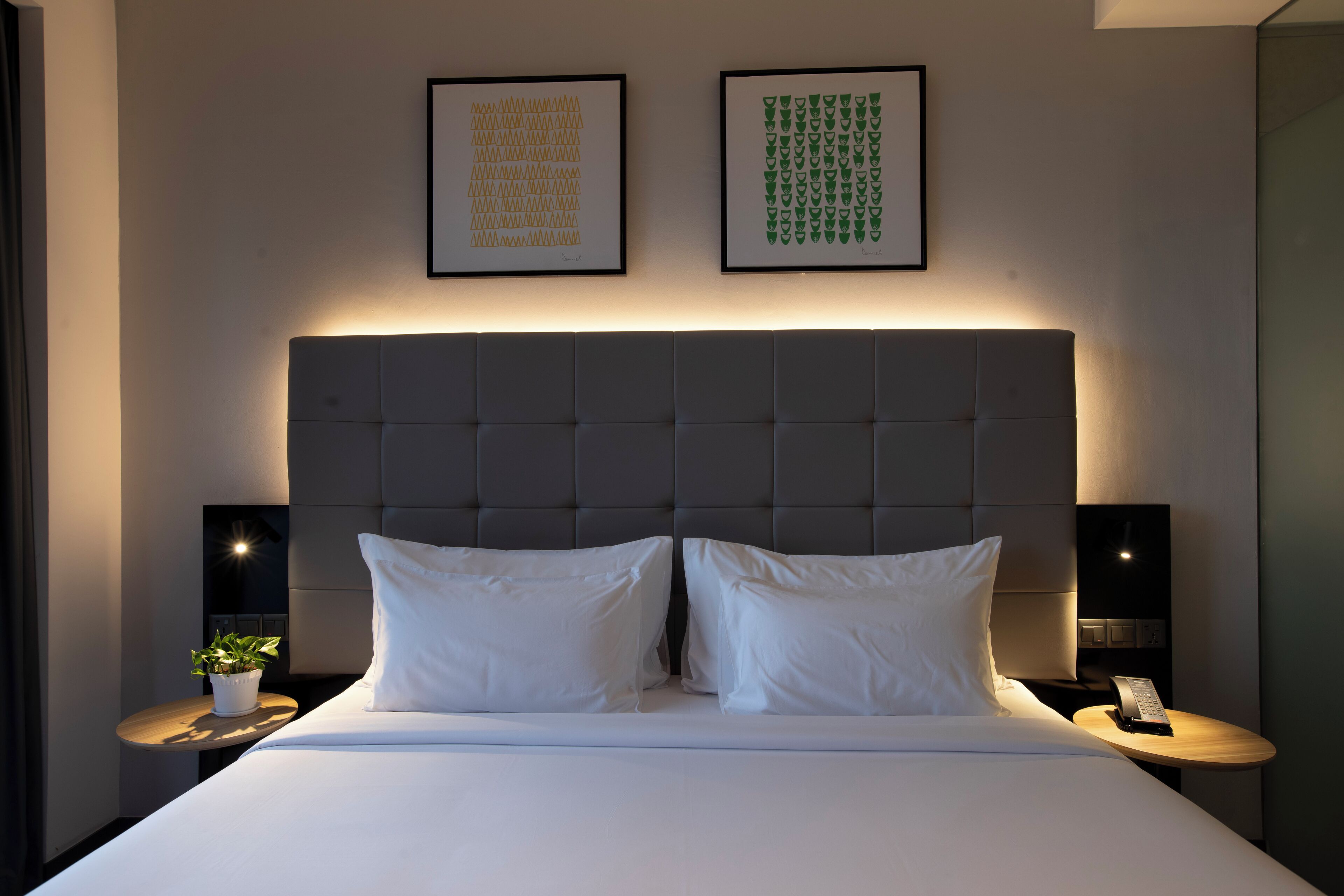 Ein modernes Hotelzimmer mit einem großen Bett, zwei Nachttischen, einer Kopfteil und zwei gerahmten Kunstwerken an der Wand.