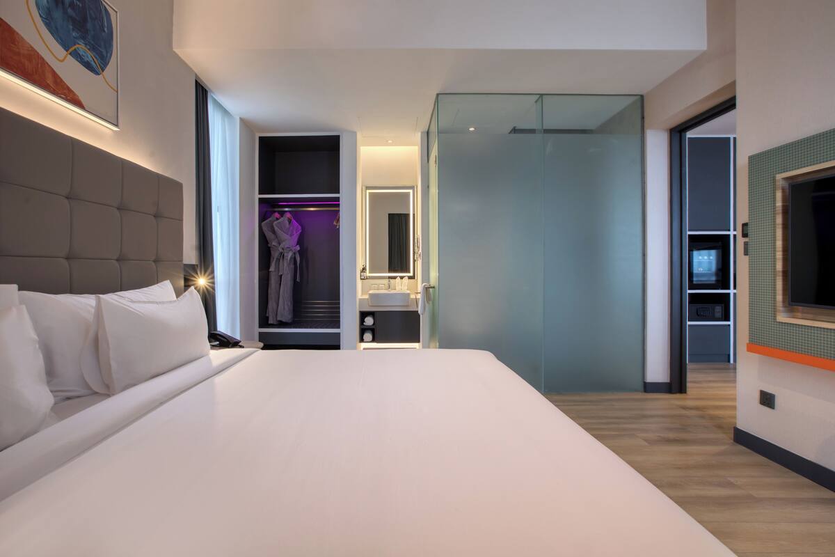 Une chambre d’hôtel moderne dotée d’un grand lit, d’un dressing, d’une salle de bain et d’une cloison en verre.