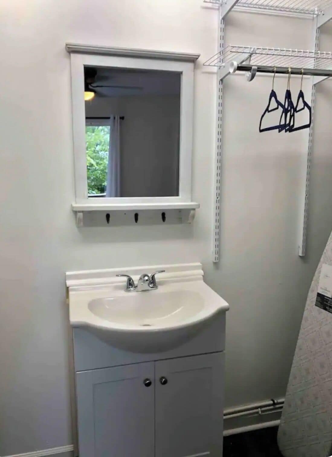 Une salle de bain avec un lavabo blanc, un miroir au-dessus, et une étagère en métal avec des porte-manteaux.