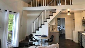 Un vaste loft doté d’un haut plafond, d’un escalier menant à un niveau supérieur, d’un coin repas avec une table et des chaises, et d’un espace cuisine.