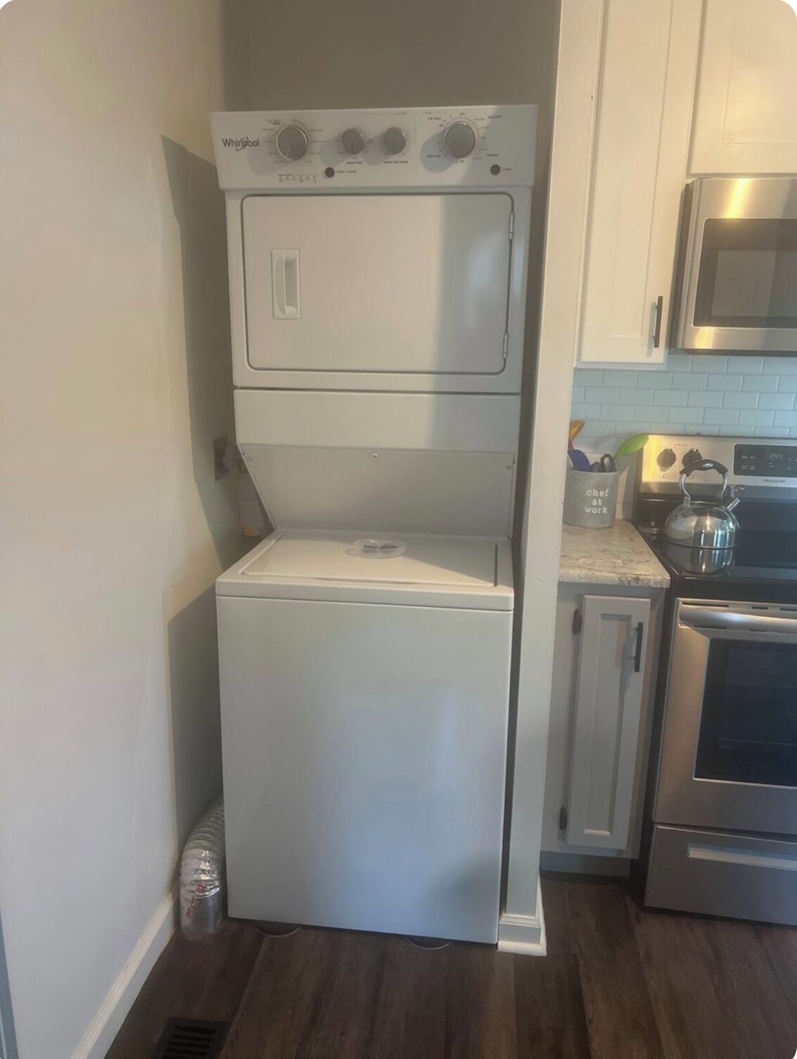 A compact washer and dryer unit in a kitchen with white cabinets and stainless steel appliances.