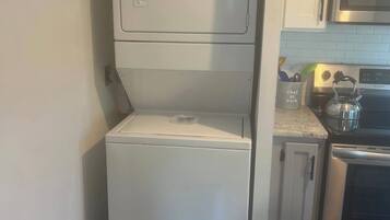 A compact washer and dryer unit in a kitchen with white cabinets and stainless steel appliances.