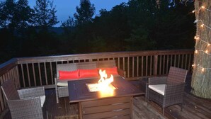 Une terrasse extérieure avec des meubles en osier, un foyer et des guirlandes lumineuses.