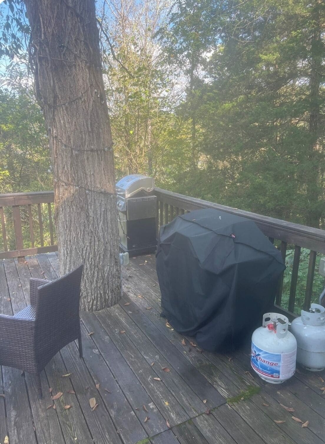 A wooden deck with a grill and a covered barbecue, a wicker chair, and propane tanks.