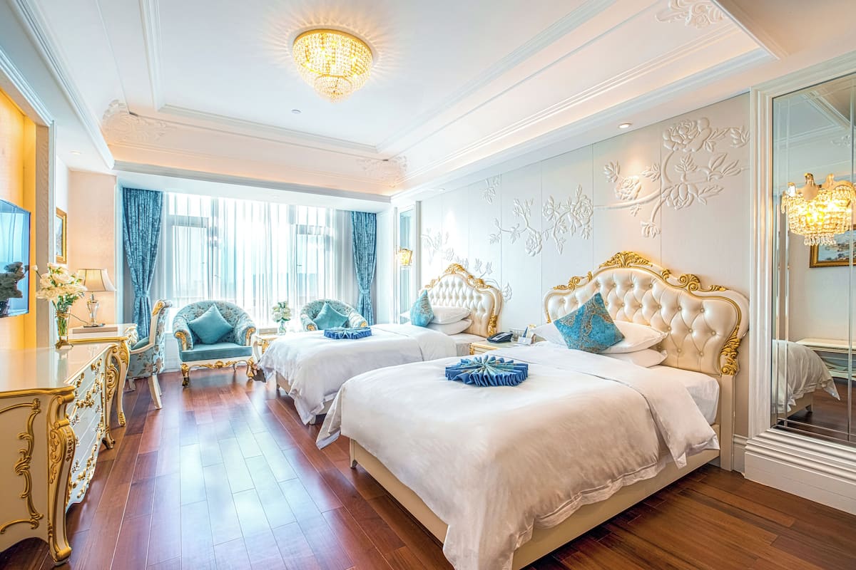 Quarto de hotel luxuoso com duas camas grandes, mobiliário requintado e um candelabro.