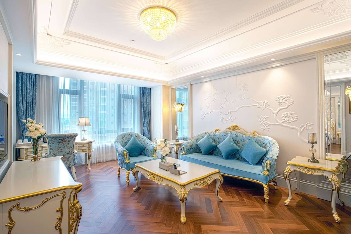 Uma sala de estar luxuosa com móveis ricamente decorados, um candelabro e uma janela grande com cortinas.