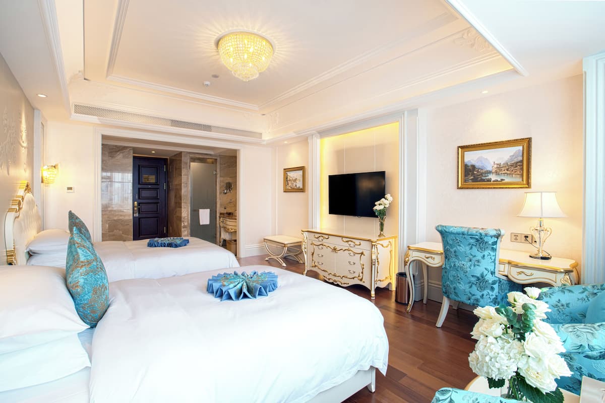 Quarto de hotel com duas camas, uma escrivaninha, uma cadeira, uma televisão e um quadro na parede.