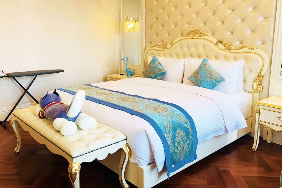 Um quarto luxuoso com cabeceira estofada, um banquinho com um brinquedo macio e uma mesinha de cabeceira com abajur.