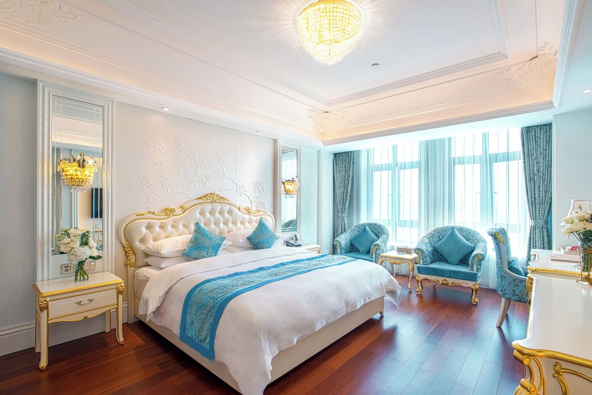 Um quarto luxuoso com uma cama grande, duas poltronas, uma toucador e um candelabro.