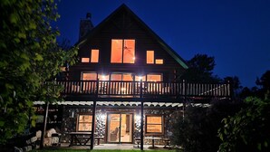 Une maison en bois à deux étages, dotée d’un balcon, de grandes fenêtres et d’une façade en pierre.