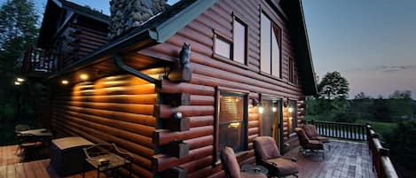 A log cabin with a deck, outdoor seating, and a stone chimney.